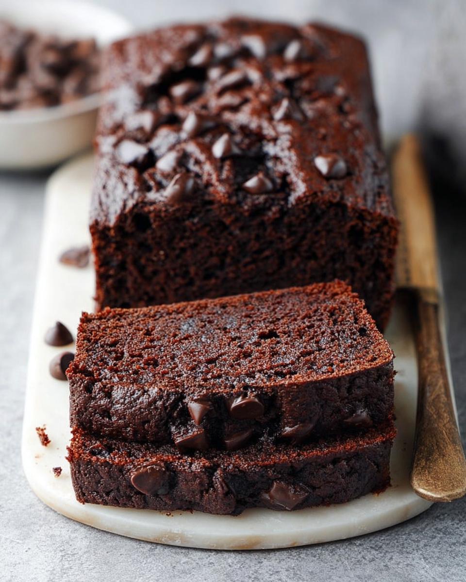 Two thick slices of moist Chocolate Banana Bread, topped with melted chocolate chips, resting in front of the loaf.