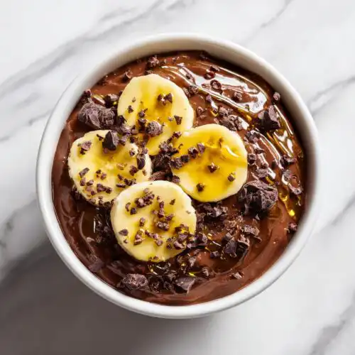Overhead view of rich Overnight Oats Chocolate topped with banana slices, cacao nibs, and a drizzle of honey.
