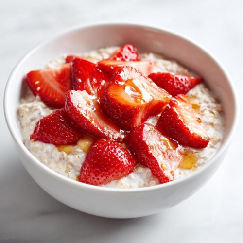 A close-up of creamy Overnight Oats Strawberry topped with fresh sliced strawberries and a drizzle of honey.