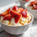 A close-up of creamy Overnight Oats Strawberry topped with fresh sliced strawberries and a drizzle of honey.