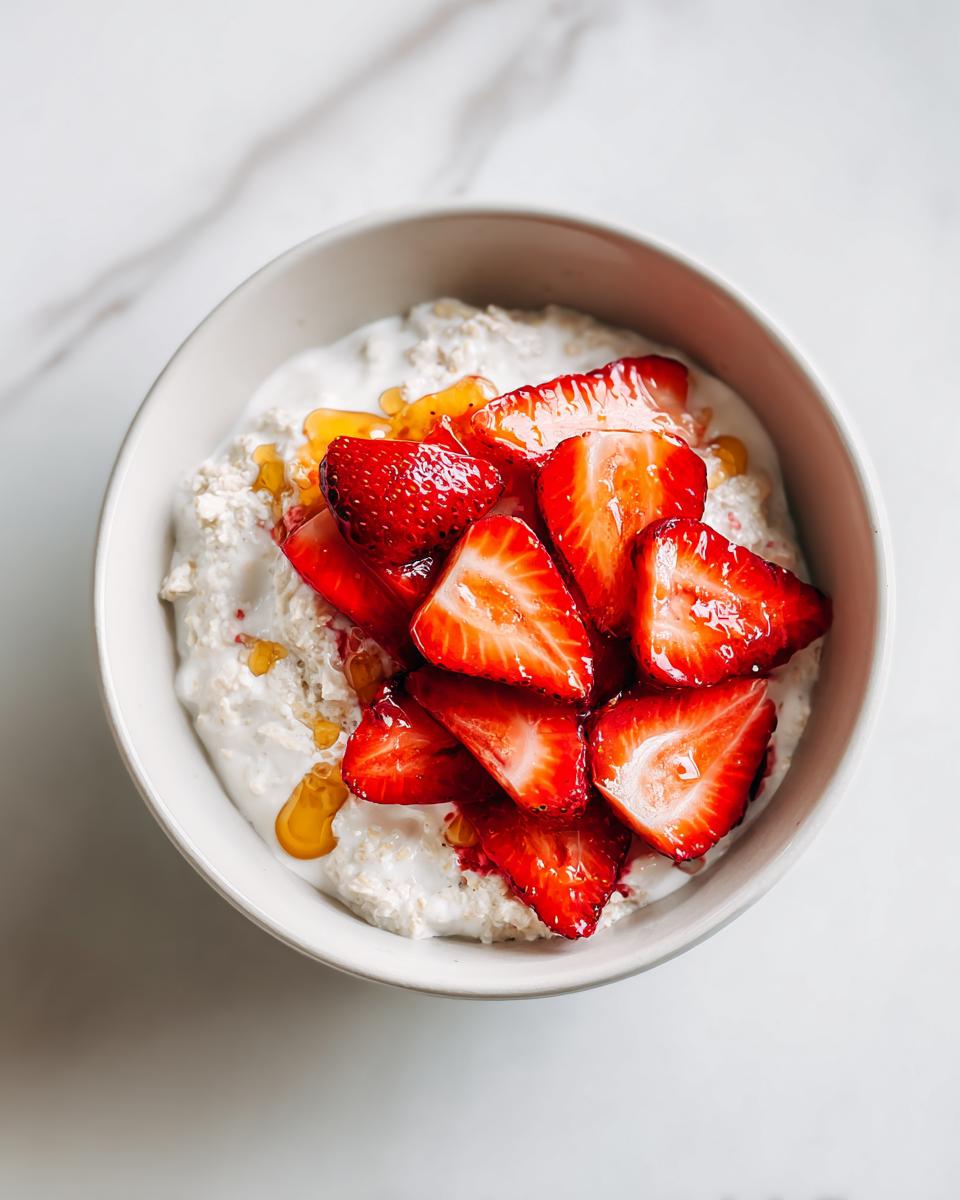 Overhead view of Overnight Oats Strawberry topped with fresh sliced strawberries and a drizzle of honey.