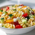 Close-up of vibrant Pasta Salad Picnic Style featuring rotini pasta, chopped cucumbers, cherry tomatoes, and crumbled feta cheese.