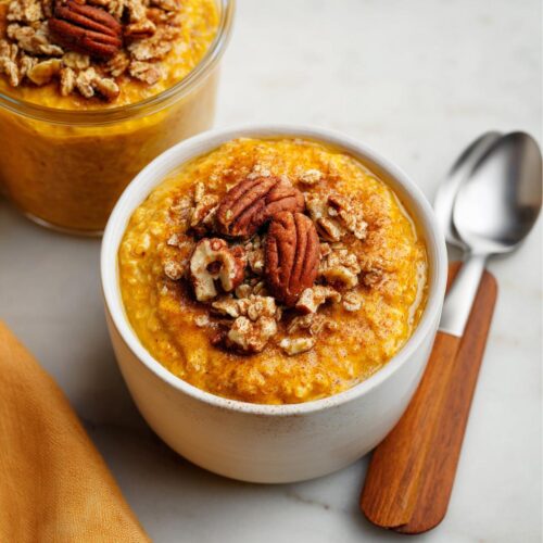 A close-up of Pumpkin Pie Overnight Oats topped with pecans and cinnamon in a white bowl.