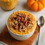 A close-up of a bowl of creamy Pumpkin Pie Overnight Oats topped with pecans and oats.