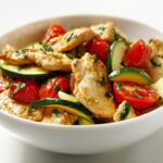 Close-up of a white bowl filled with Quick Summer Chicken Skillet, featuring sliced chicken, zucchini, and cherry tomatoes.