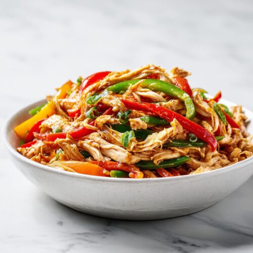 A white bowl filled with shredded chicken mixed with colorful strips of red, green, and yellow peppers, perfect for Summer Crockpot Dinner Ideas.