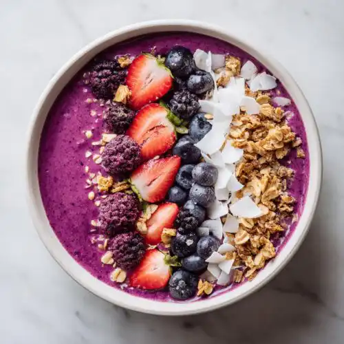 Overhead view of a vibrant purple smoothie bowl featuring strawberries, blueberries, blackberries, granola, and coconut flakes, showcasing Smoothie Bowl Aesthetic.