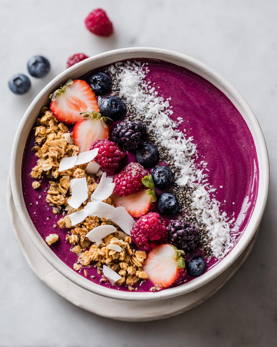 Overhead shot of a vibrant purple Smoothie Bowl Aesthetic topped with granola, coconut flakes, strawberries, blueberries, and raspberries.