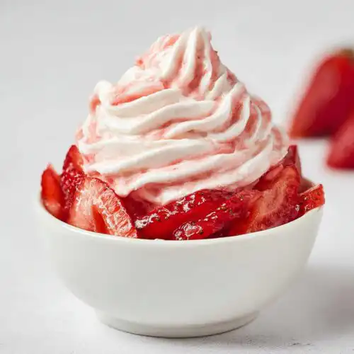 A white bowl filled with sliced strawberries topped with a swirl of pink and white strawberry cream dessert.