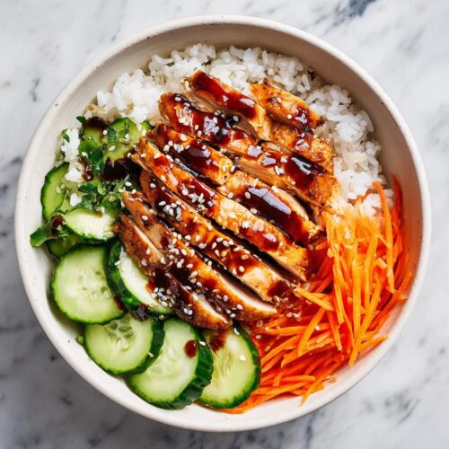 Overhead view of a Summer Chicken and Rice Bowl featuring sliced glazed chicken, white rice, cucumbers, and shredded carrots.