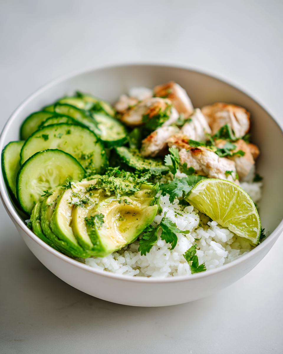Close-up of a Summer Chicken Avocado Bowl featuring white rice, sliced avocado, grilled chicken, cucumber, and a lime wedge.