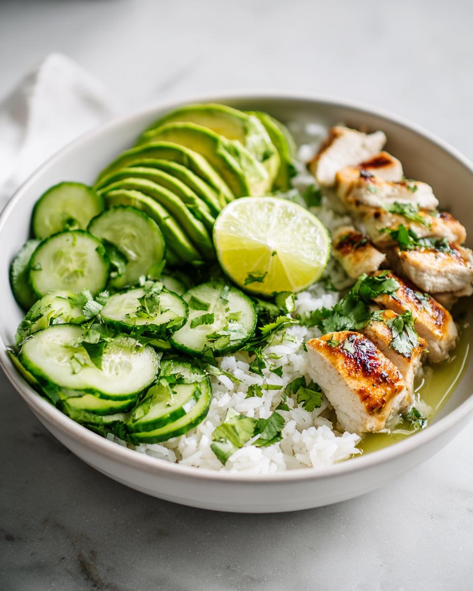 Close-up of a Summer Chicken Avocado Bowl featuring grilled chicken, sliced avocado, cucumbers, and lime over rice.