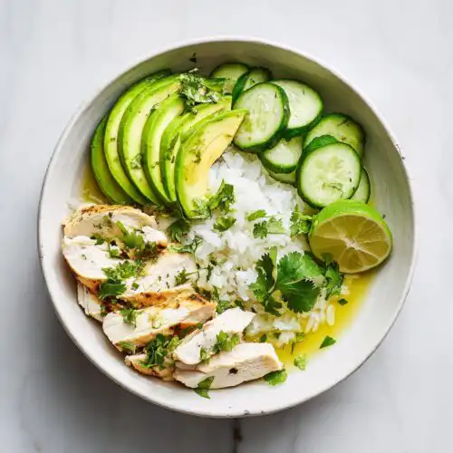 Overhead view of a Summer Chicken Avocado Bowl featuring sliced grilled chicken, white rice, avocado, cucumber, and lime.