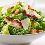 Close-up of a fresh Summer Chicken Caesar Salad featuring grilled chicken slices, romaine lettuce, croutons, and Parmesan shavings.