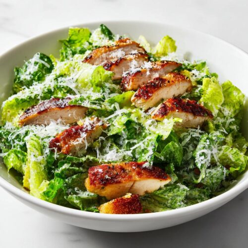 A close-up of a Summer Chicken Caesar Salad featuring grilled chicken slices, crisp romaine, and grated Parmesan cheese.