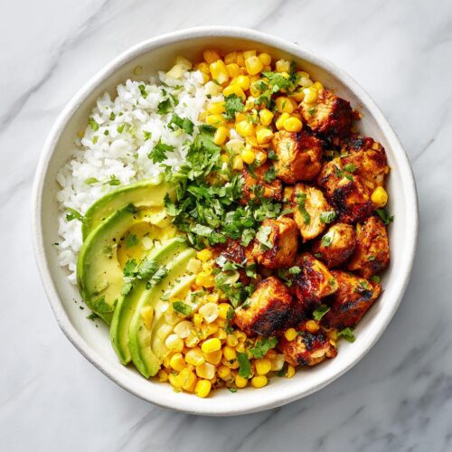 Overhead view of a Summer Chicken Corn Bowl featuring seasoned chicken, white rice, corn, and sliced avocado.