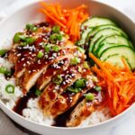 Close-up of a Summer Chicken Rice Bowl featuring sliced, glazed chicken breast over white rice with shredded carrots and cucumber slices.