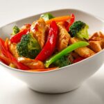 Close-up of a colorful Summer Chicken Stir Fry featuring glazed chicken pieces, bright red peppers, and green broccoli florets.