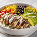 A vibrant Summer Chicken Taco Bowl featuring sliced grilled chicken, avocado, corn, black beans, and white sauce over rice.