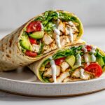Two halves of a delicious Summer Chicken Wrap filled with grilled chicken, avocado, tomato, and lettuce, drizzled with white sauce.