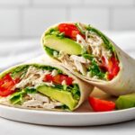Two halves of a fresh Summer Chicken Wrap Lunch showing shredded chicken, avocado slices, tomato, and lettuce.