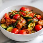 A white bowl filled with Summer Crockpot Easy Recipes featuring chicken chunks, zucchini slices, and bright red cherry tomatoes.