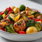 A vibrant bowl of roasted chicken pieces mixed with potatoes, zucchini, broccoli, and red peppers, perfect for summer dinner ideas.