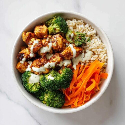 Overhead view of a Summer Meal Prep Bowl containing brown rice, glazed chicken pieces, bright green broccoli, and shredded carrots with a creamy drizzle.
