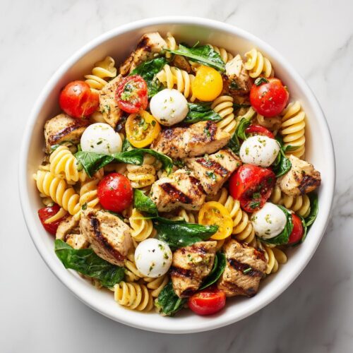 Overhead view of a Summer Pasta Bowl featuring fusilli, grilled chicken pieces, cherry tomatoes, and mozzarella balls.