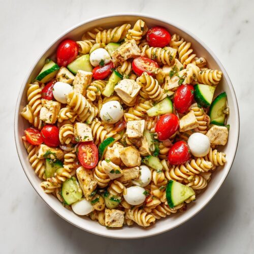 Overhead view of a Summer Pasta Salad with Chicken featuring rotini pasta, cherry tomatoes, cucumber, and mozzarella balls.