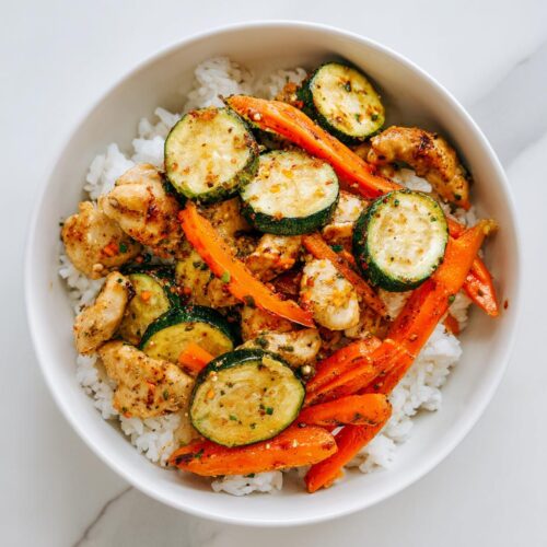 Overhead view of a Summer Veggie Bowl with Chicken, featuring seasoned chicken pieces, sliced zucchini, and carrots served over white rice in a white bowl.