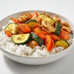 A close-up of a Summer Veggie Bowl with Chicken featuring sautéed zucchini and carrots served over white rice in a light bowl.