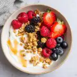 Overhead view of an aesthetic Yogurt Bowl with Fruits, topped with mixed berries, granola, and a drizzle of honey.