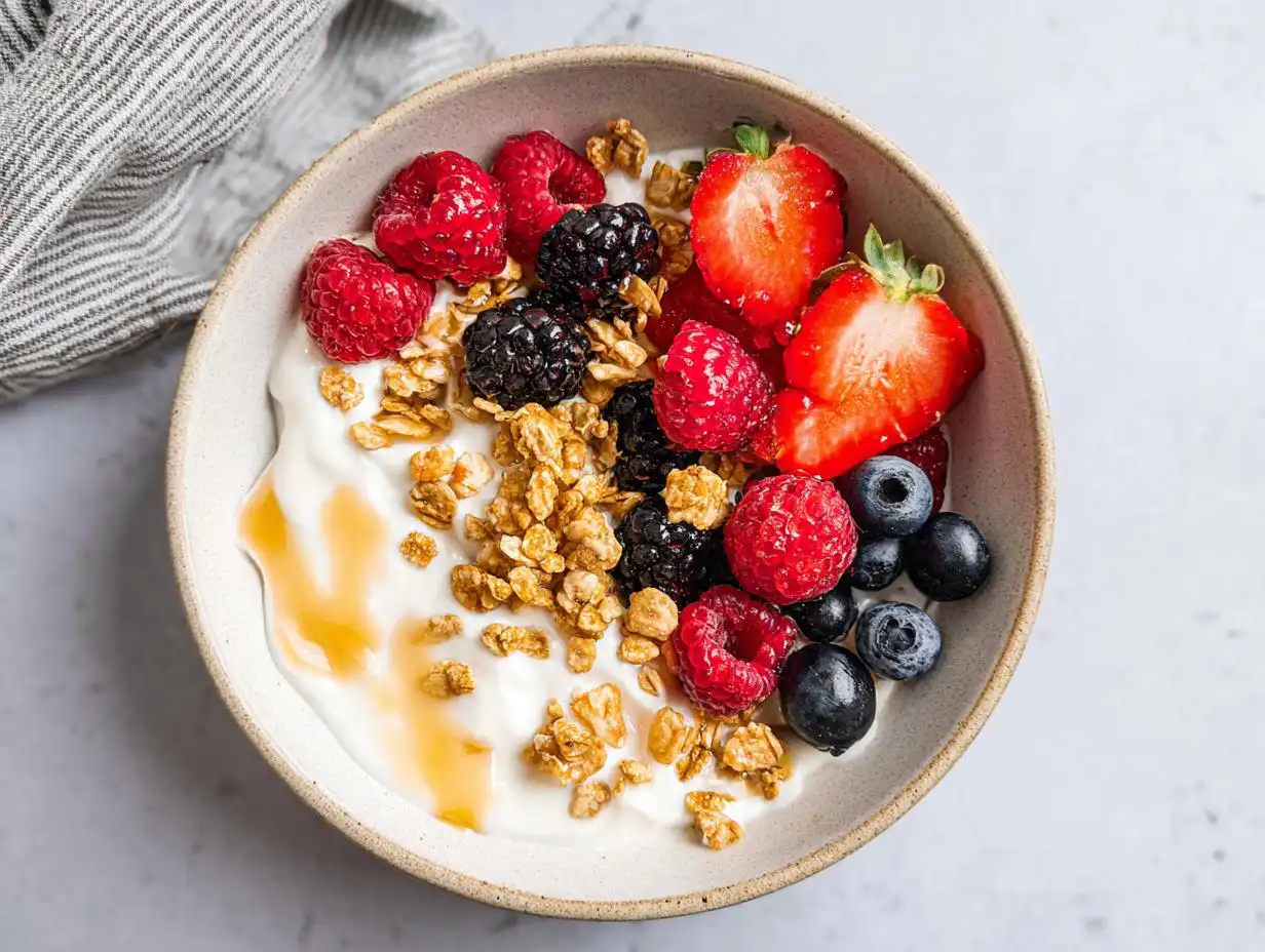 Overhead view of an aesthetic Yogurt Bowl with Fruits, topped with mixed berries, granola, and a drizzle of honey.