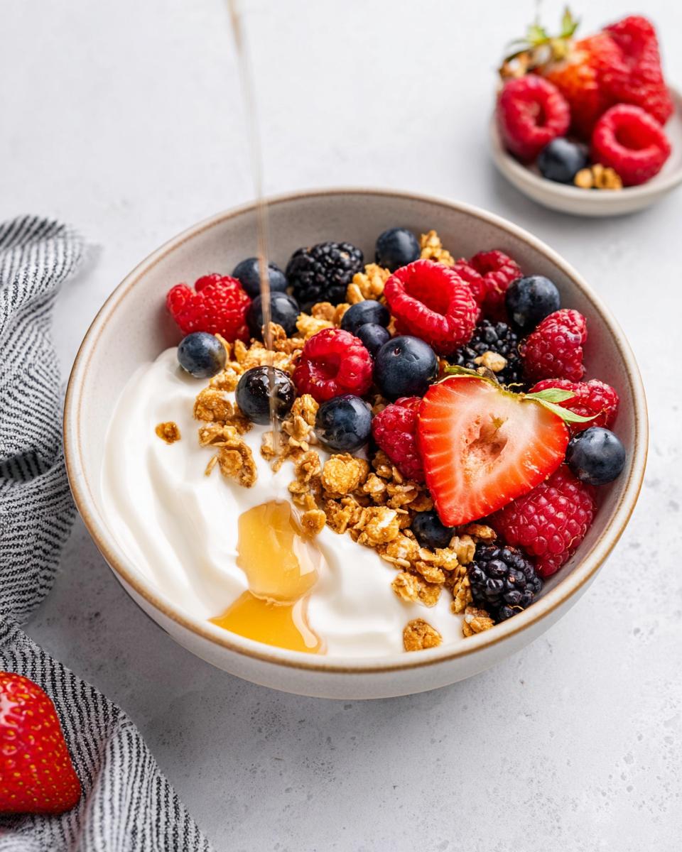 Close-up of an aesthetic Yogurt Bowl with Fruits, granola, and honey being drizzled on top.