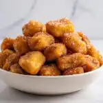 A white bowl overflowing with golden brown Air Fryer Churro Nuggets generously coated in sparkling cinnamon sugar.
