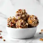 Close-up of several Bacon Ranch Cheese Ball Bites coated in chopped nuts and seeds, served in a small white bowl.