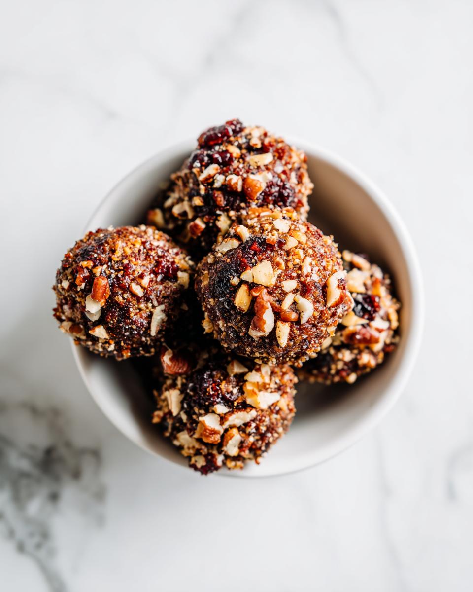 Close-up overhead view of several Bacon Ranch Cheese Ball Bites coated in chopped nuts and dried fruit, served in a small white bowl.