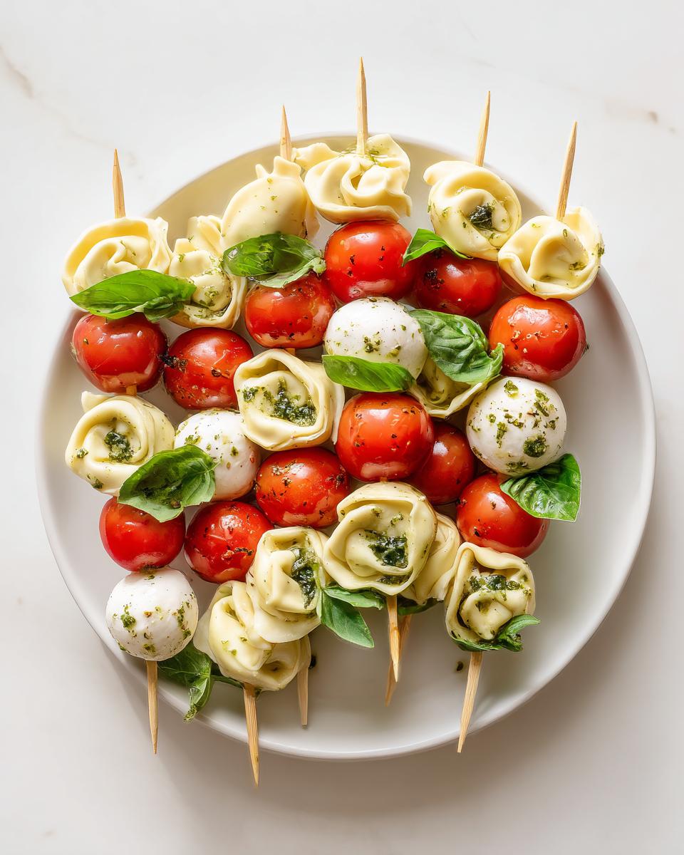 Close-up of several Cheesy Tortellini Kabobs featuring tortellini, cherry tomatoes, mozzarella balls, and basil leaves on skewers.