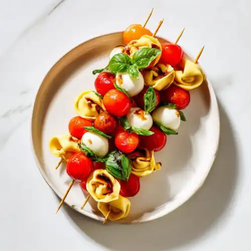 Close-up of several Cheesy Tortellini Kabobs featuring tortellini, cherry tomatoes, mozzarella balls, and basil leaves on a plate.
