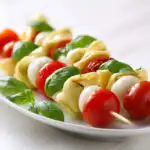 Close-up of Cheesy Tortellini Kabobs featuring tortellini, mozzarella balls, cherry tomatoes, and fresh basil leaves on skewers.