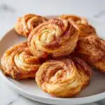 A close-up of several golden-brown Churro Cream Cheese Swirls dusted with cinnamon sugar on a white plate.