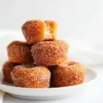 A stack of golden brown Churro Muffin Bites generously coated in cinnamon sugar, resting on a white plate.