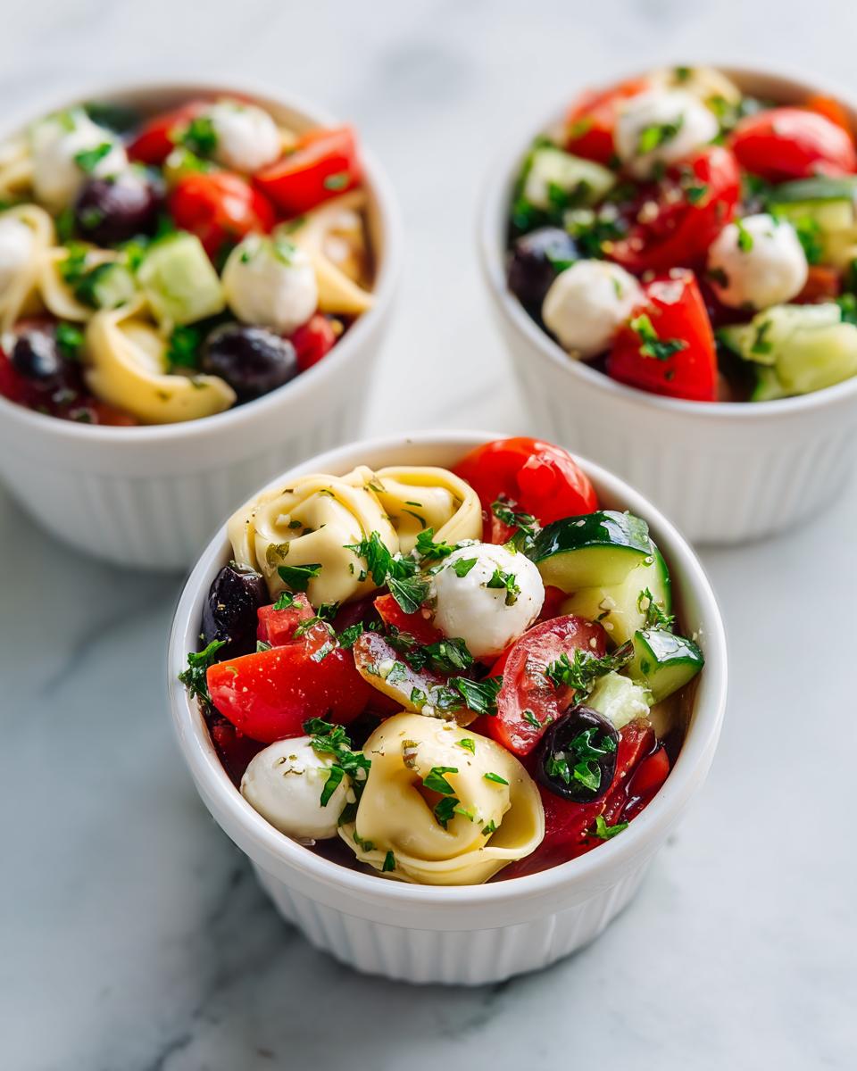 Three servings of Italian Dressing Tortellini Salad Cups featuring tortellini, mozzarella balls, tomatoes, cucumbers, and olives.