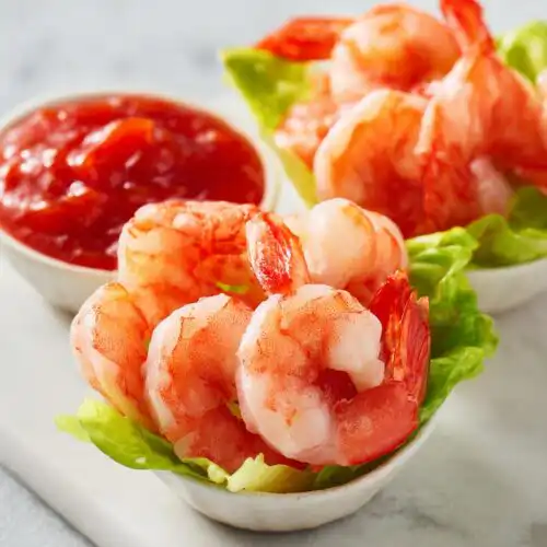 Close-up of prepared Shrimp Cocktail Cups served on lettuce with a side of bright red cocktail sauce.