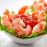 A white cup filled with crisp lettuce, bright red cocktail sauce, and perfectly arranged cooked shrimp for Shrimp Cocktail Cups.